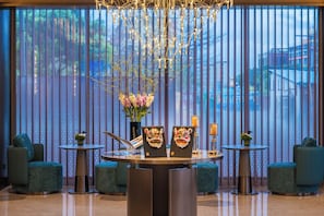 A modern lobby with a round table, two chairs, a vase with flowers, and a decorative mask.