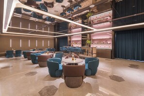 Un espace lounge moderne avec des tables rondes, des chaises bleues et un bar doté d’étagères remplies de bouteilles.
