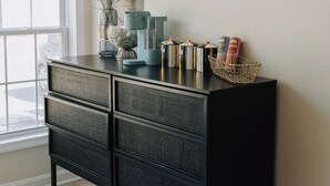 Una consola negra amb diversos calaixos, una màquina de cafè i objectes decoratius sobre un moble penjat a la paret.