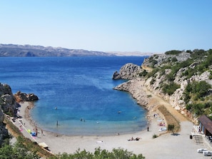 Ein Strand mit klarem, blauem Wasser, felsigen Klippen und einigen Personen.