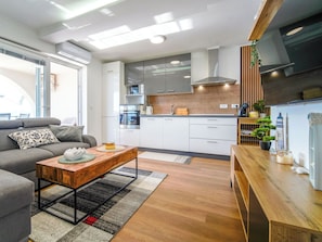 Ein modernes Wohnzimmer mit einer Couch, einem Couchtisch und einer Küchenzeile inklusive Schränken und Geräten.