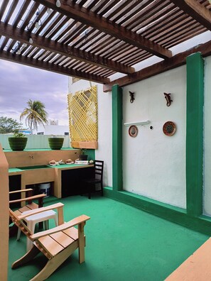 A covered patio with a wooden ceiling, a green floor, a table with chairs, and decorative plates on the wall. - Capitan Tiega House (Isla Mujeres)
