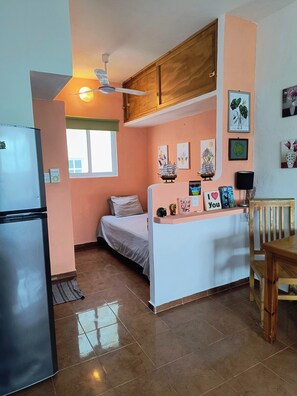 A compact kitchen with a refrigerator, a bed, a dining table, and a ceiling fan. - Capitan Tiega House (Isla Mujeres)