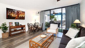 Una sala de estar con un sofá, una mesa de centro de vidrio, una zona de comedor con sillas, una consola de madera y un cuadro en la pared.