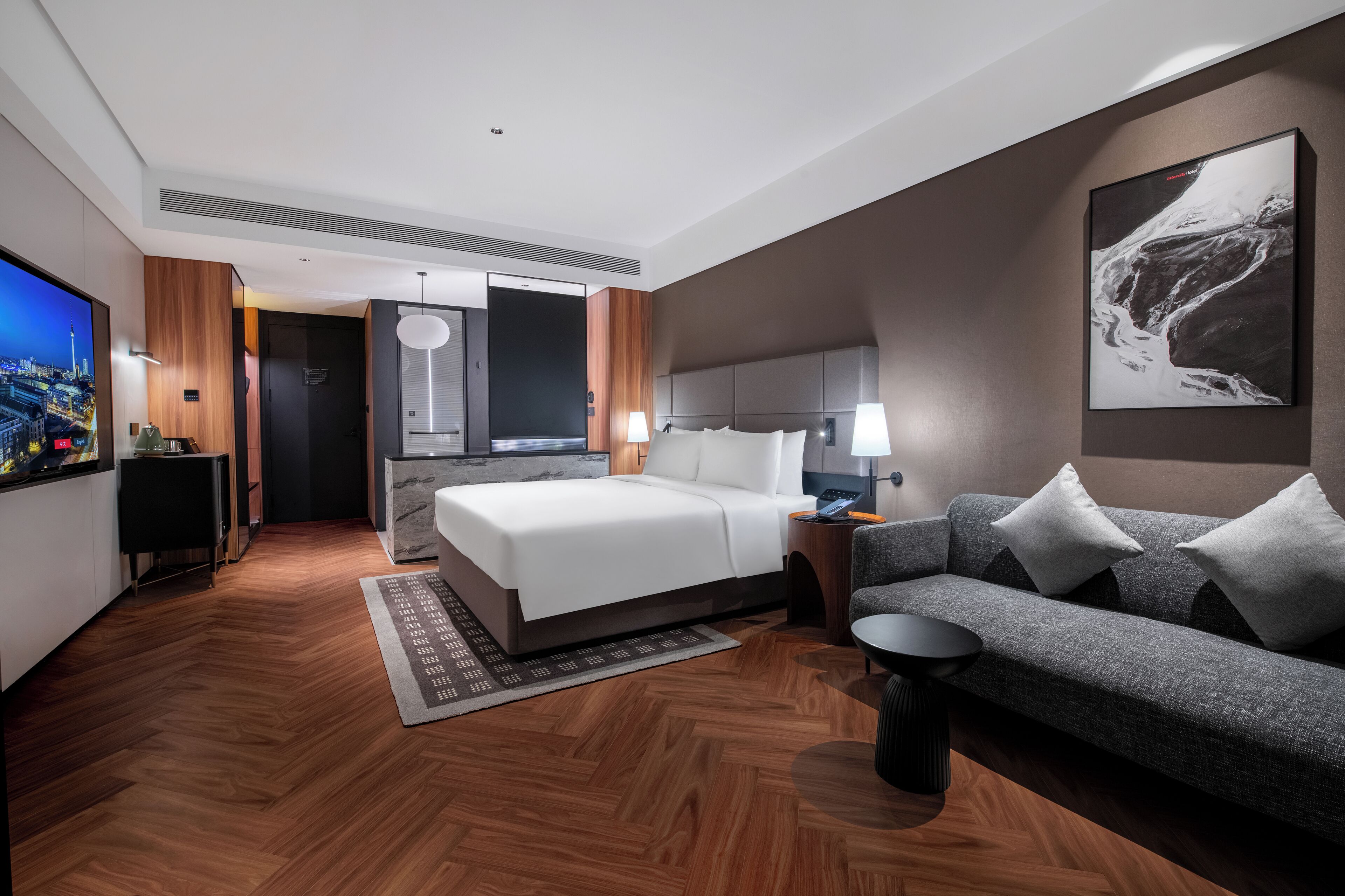 A modern hotel room with a bed, a sofa, a TV, and a large painting on the wall.
