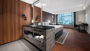 Una habitación de hotel moderna con una pared de madera, una cama grande, un tocador empotrado y un ventanal con vistas a la ciudad.