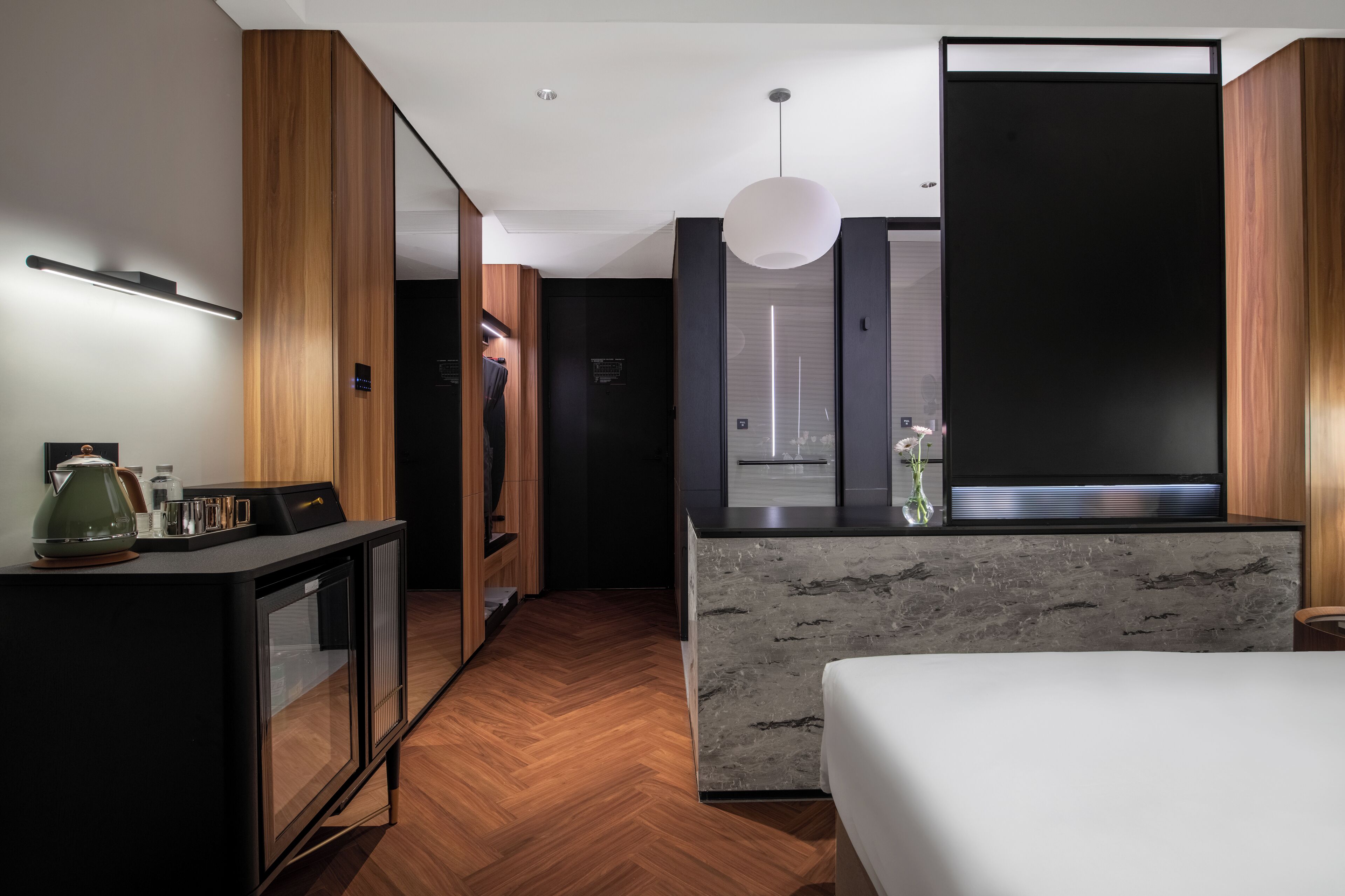 A modern hotel room with a bed, a desk with a coffee maker, a TV, and a large window.