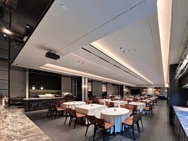 A modern restaurant with round tables and chairs, a marble counter, and recessed lighting on the ceiling.