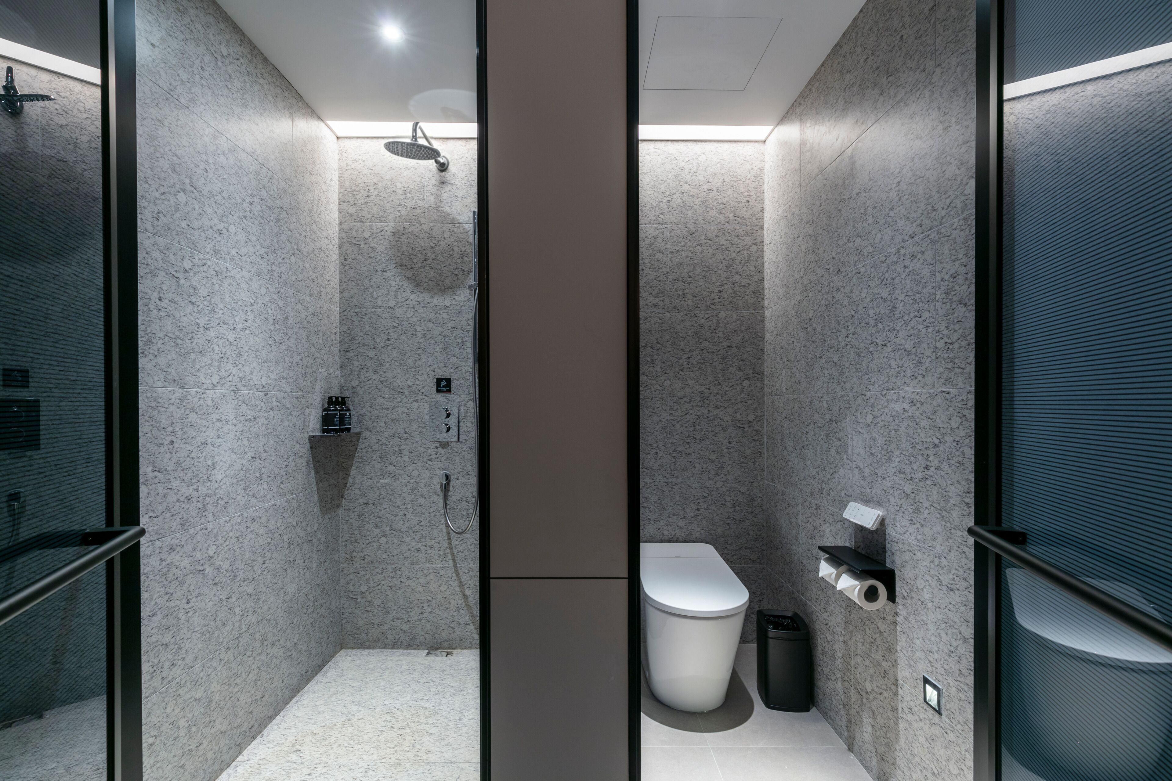 A modern bathroom with a shower, toilet, and a trash bin.