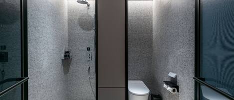 A modern bathroom with a shower, toilet, and a trash bin.