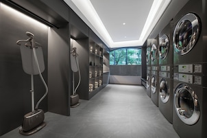 A modern laundry facility with multiple washing machines, a steam cleaner, and a large window providing a view of trees.