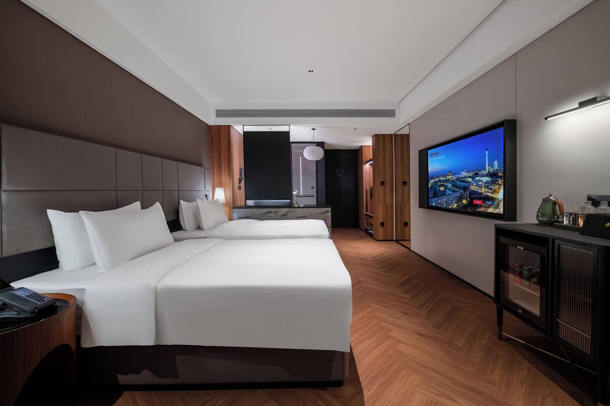 Moderni hotellihuone, jossa on suuri sänky, televisio ja puulattia.