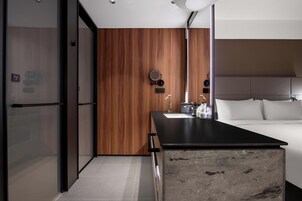 Una habitación de hotel moderna con una pared de madera, una encimera negra, una cama con ropa blanca y un espejo grande.
