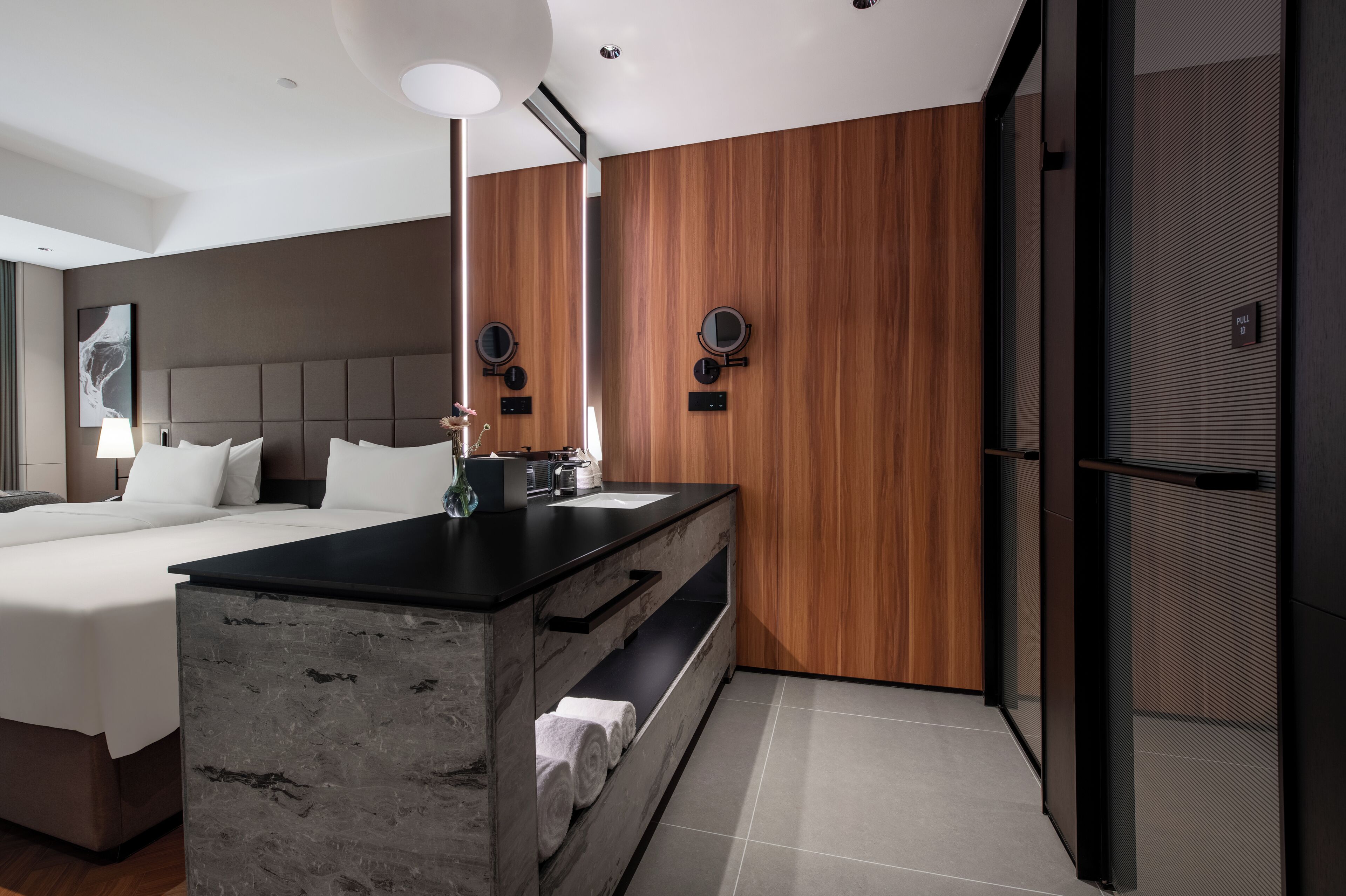 Une chambre d’hôtel moderne dotée d’un grand lit, d’un mur décoratif en bois, d’une coiffeuse intégrée et d’un grand miroir.