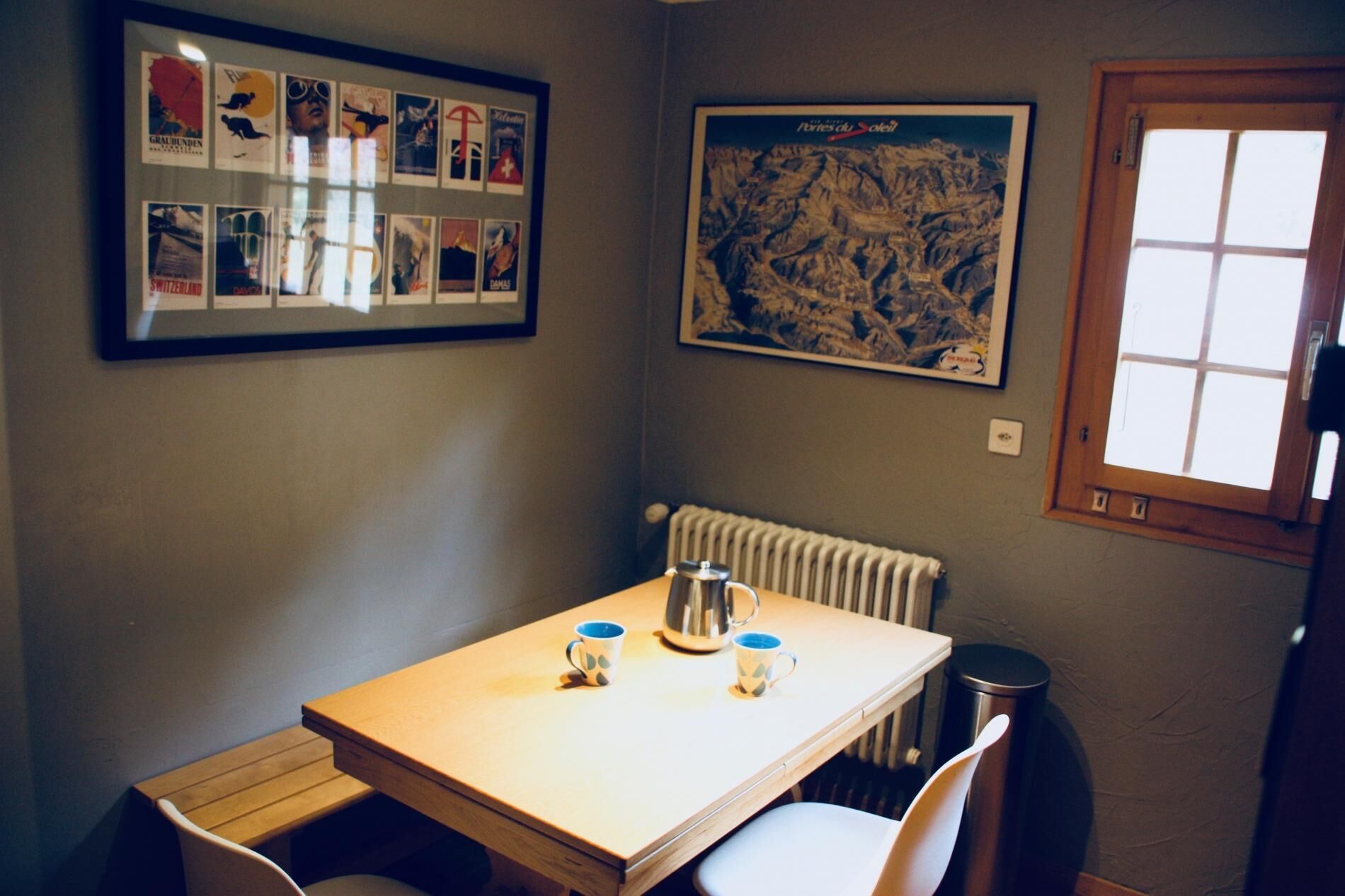 Un pequeño comedor con una mesa, sillas, un radiador y una ventana.