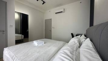 A hotel room with a bed, a desk, a chair, a mirror, and an air conditioning unit.