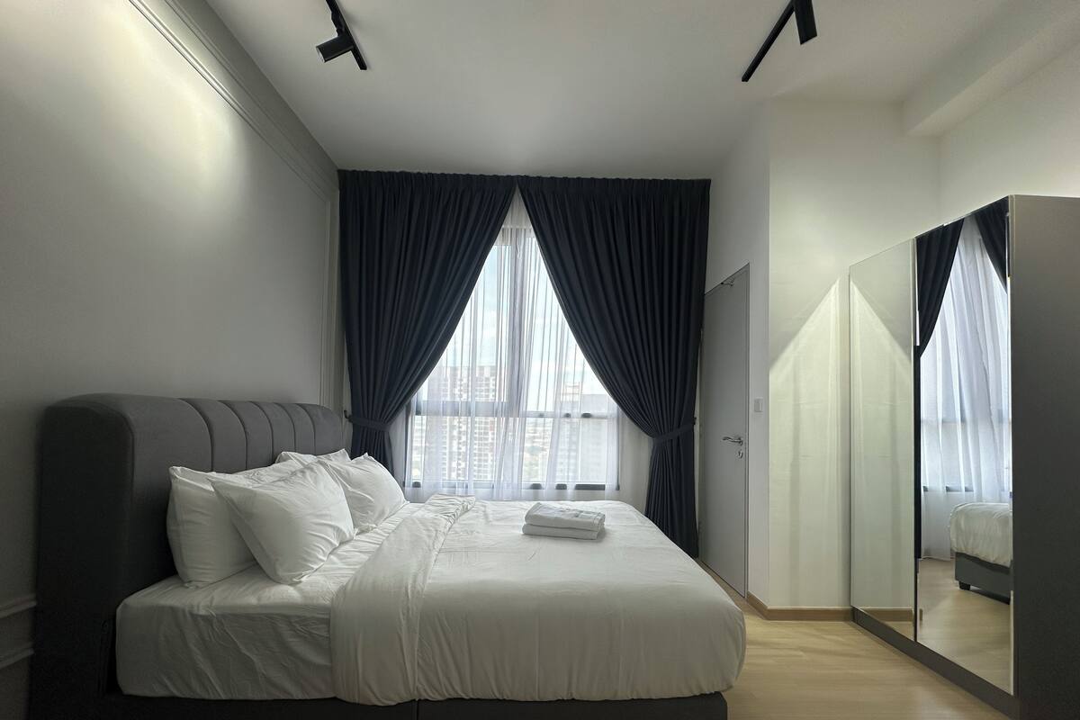 Un dormitorio moderno con una cama grande, cortinas oscuras, un armario y un espejo.