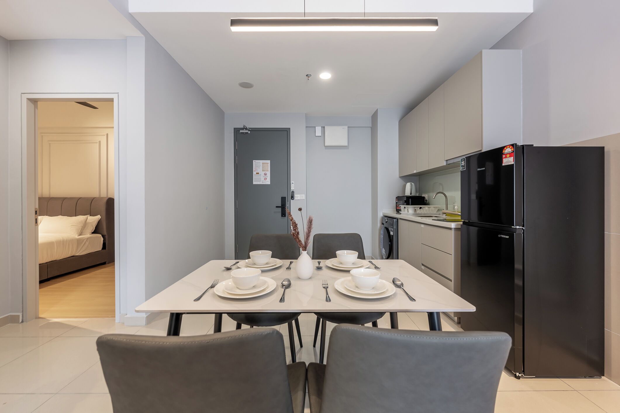 Una cocina moderna con un refrigerador negro, una mesa de comedor con platos blancos y cubiertos, y un sofá gris en la zona de estar contigua.