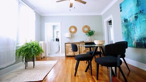 Un comedor con ventilador de techo, una mesa de comedor con sillas, una planta en maceta y un cuadro abstracto grande en la pared.