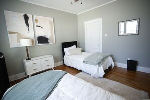 A bedroom with two beds, a white dresser, a mirror, and abstract wall art. - Charming Midtown home in the heart of Memphis (Memphis)