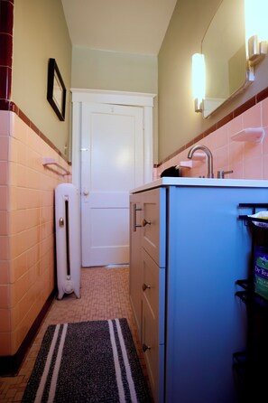 A narrow bathroom with a white door, a sink with a mirror, and a towel rack. - Charming Midtown home in the heart of Memphis (Memphis)