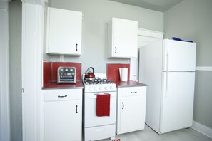 A compact kitchen with white cabinetry, a gas stove, an oven, and a refrigerator. - Charming Midtown home in the heart of Memphis (Memphis)