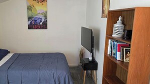 A bedroom with a bed, a TV on a stand, a bookshelf, and a poster on the wall.