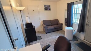A room with a white door, a gray sofa, a standing lamp, a white speaker, and a white air purifier.