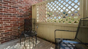 Une terrasse avec un mur en briques, une clôture en bois ornée d’un motif en treillis et deux chaises en métal.