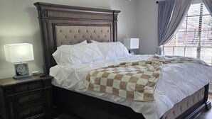 Une chambre à coucher avec un lit en bois, une table de chevet avec une lampe, un ventilateur de plafond et une fenêtre avec des rideaux.