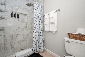 Een badkamer met een douche, toilet en een mandje op het toilet.