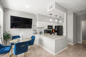 Een moderne keuken met een centraal eiland, witte kasten en een flatscreen televisie aan de muur.