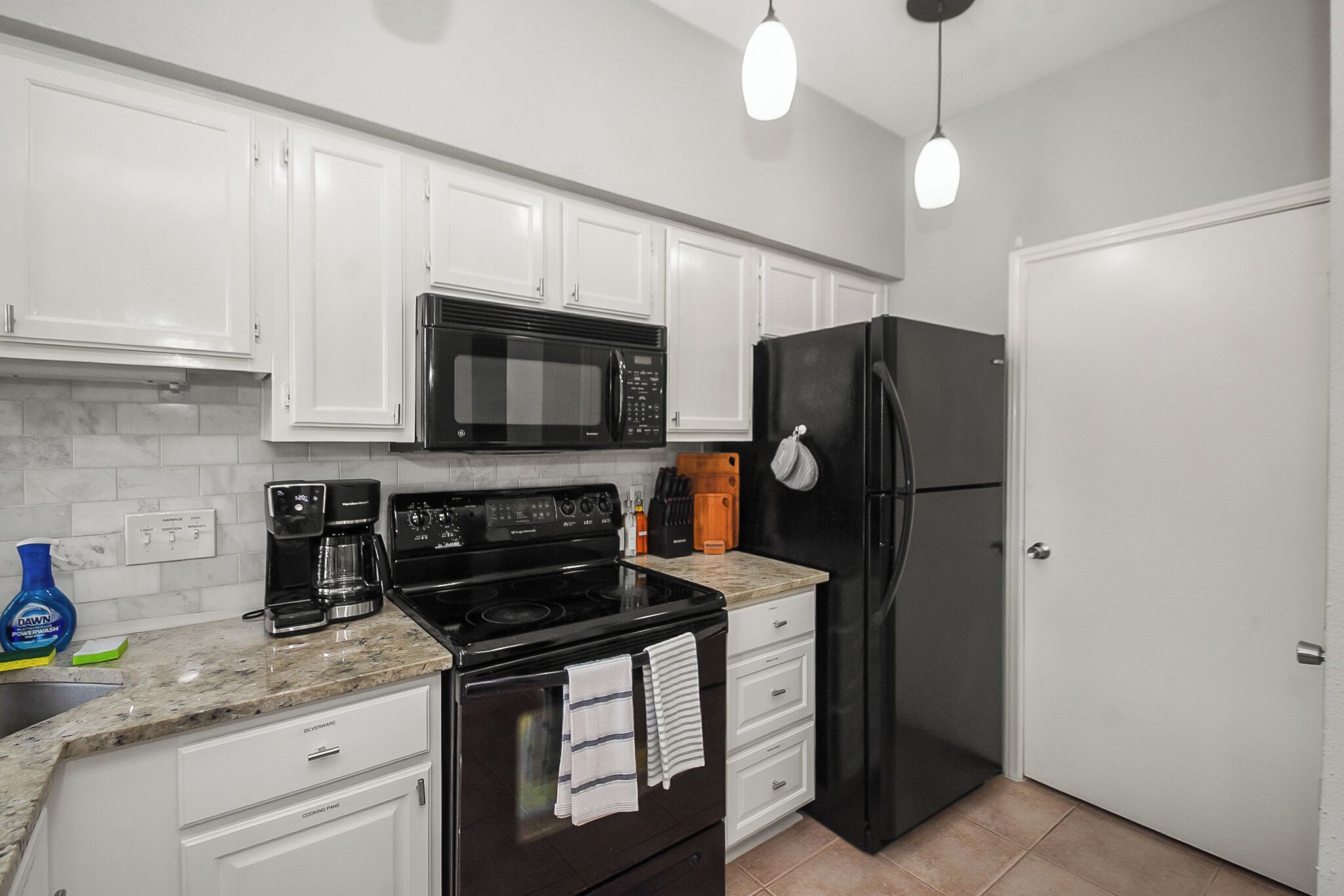 A kitchen with white cabinets, a black stove, a microwave, and a refrigerator.