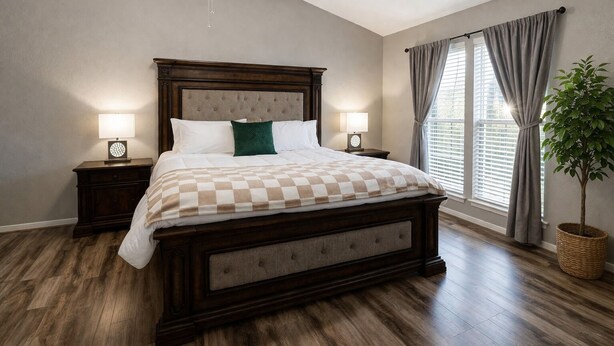 Une chambre à coucher avec un grand lit, deux tables de chevet, un ventilateur de plafond, une fenêtre avec des rideaux et une plante en pot.