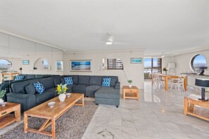 Ein modernes Wohnzimmer mit einer Eckcouch, Holz-Couchtischen und einem Essbereich mit rundem Tisch und Stühlen.