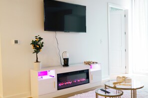 A modern living room with a flat-screen TV, fireplace, white console, and a small table with decorative items. - skyline- view+ Cozy 1BR in vibrant Atlanta (Atlanta)