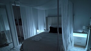 Ein Himmelbett mit durchsichtigen Vorhängen, ein Nachttisch mit Lampe und Blick ins Freie.