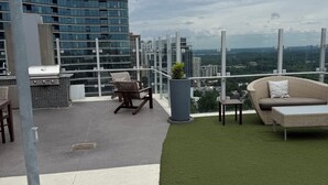 Eine Dachterrasse mit Grill, Sitzgelegenheit und Blick auf die Stadtlandschaft.