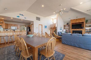 Un vaste espace de vie comprenant une table à manger, des chaises, un canapé, un téléviseur fixé à un mur en bois et un escalier menant à un niveau supérieur.