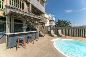 Un espace piscine doté d’une terrasse en bois, d’un bar avec des tabourets et d’un escalier menant à un balcon.
