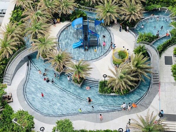 Ein großer, gewölbter Pool mit mehreren Bahnen und einer Rutsche in der Mitte, umgeben von Palmen und Grünpflanzen.