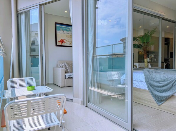 A balcony with a table and chairs, a sofa, a bed with a blanket, and a painting on the wall. - Lisa House - The Song Condotel Vung Tau  (Ho Chi Minh City)