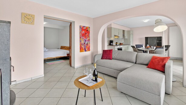 A modern living room with a sofa, a small table with a bottle and glasses, a bed, a kitchen area, and a dining table. - Panoramic Garden Lake View in Locarno Monti, Locarno, Switzerland (Locarno)