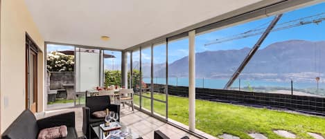 A spacious balcony with a dining area, large windows offering a view of mountains and a bridge, and a well-maintained lawn.