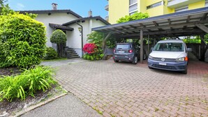 A building with a covered parking area, a white car, and a grey car parked in front. - Panoramic Garden Lake View in Locarno Monti, Locarno, Switzerland (Locarno)