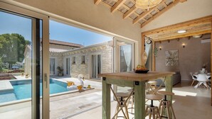 Un interior moderno con vista a la piscina, vigas de madera en el techo y un comedor con taburetes.
