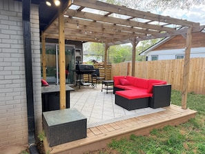 Eine überdachte Terrasse mit Grill, Gartenmöbeln und einer Holz-Pergola.