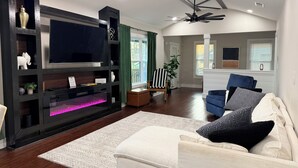 A living room with a flat-screen TV, dark wooden entertainment center, white sofa, and a ceiling fan. - 3BR House 5 Minutes from Downtown Atlanta near Mercedes Benz Stadium World Cup (Decatur)