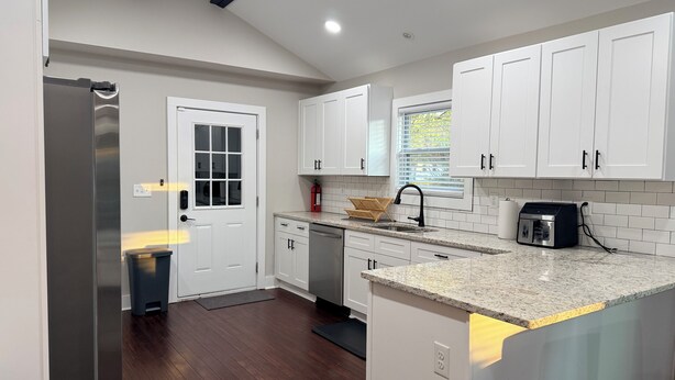 A modern kitchen with white cabinets, a stainless steel refrigerator, a built-in dishwasher, and a granite countertop. - 3BR House 5 Minutes from Downtown Atlanta near Mercedes Benz Stadium World Cup (Decatur)