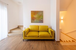 A living room with a yellow sofa, a staircase, and a colorful abstract painting on the wall. - Dar Sara Holiday Gozitan Home, IR-RABAT, Malta (IR-RABAT)